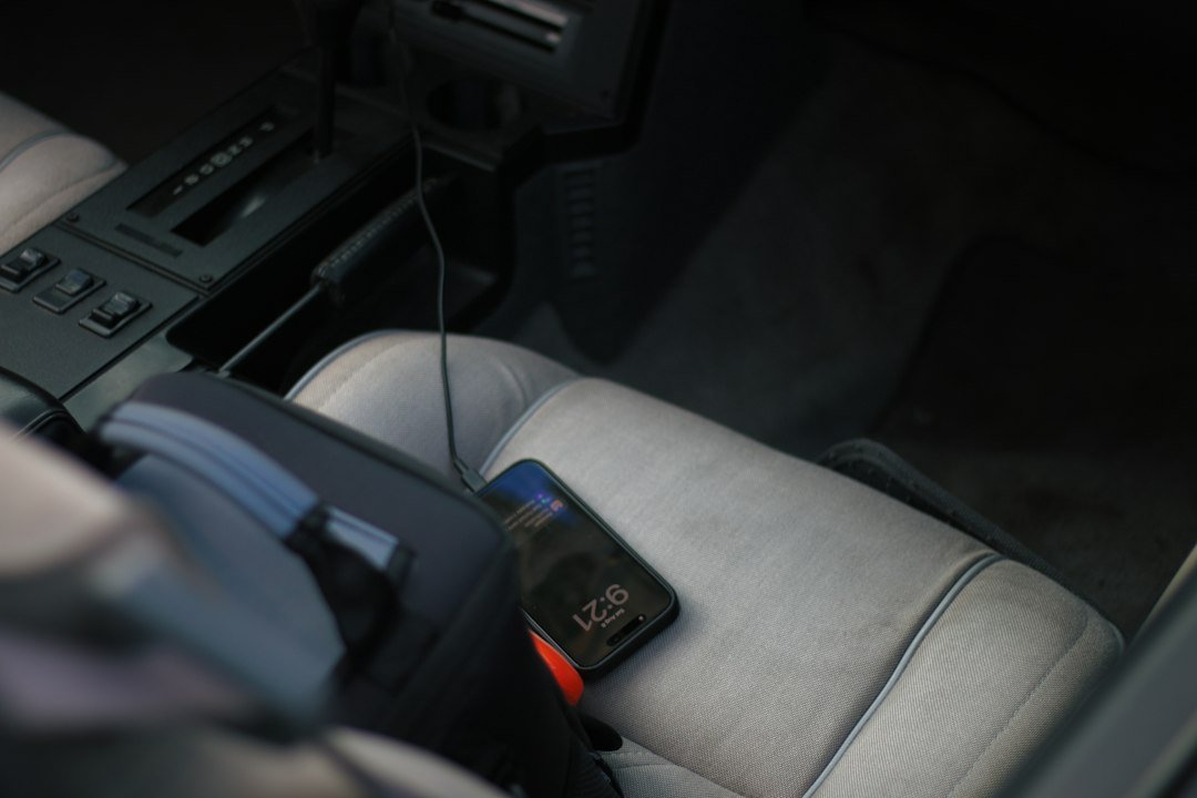A smartphone charging on a grey car seat next to a black bag